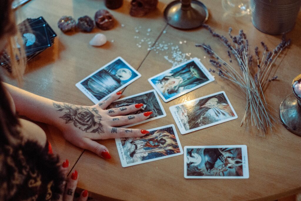 A mystical setup featuring tarot card reading on a wooden table, with artistic tattoos and dried flowers.